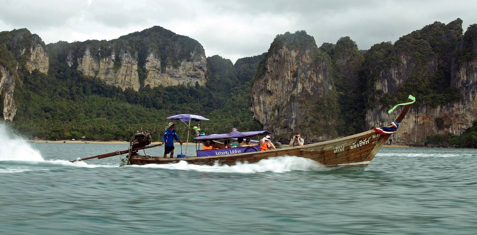 A longtail boat speeding past limestone cliffs near Railay